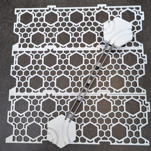 May include: White plastic tiles with a hexagonal pattern and a metal connector. The tiles are designed to be connected together to create a modular floor system.