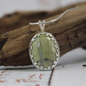 May include: Oval pendant necklace with a silver-colored setting and a green stone with white and gray veining. The pendant is suspended from a thin silver chain. The pendant is approximately 1.5 inches long.