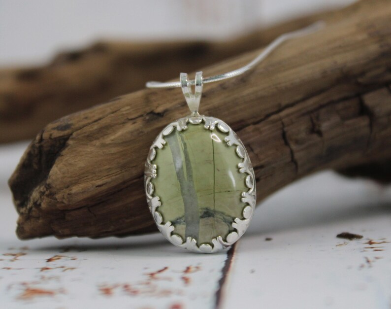May include: Oval pendant necklace with a silver-colored setting and a green stone with white and gray veining. The pendant is suspended from a thin silver chain. The pendant is approximately 1.5 inches long.
