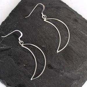 May include: A pair of silver crescent moon earrings. The earrings are made of thin wire and have a simple, elegant design.