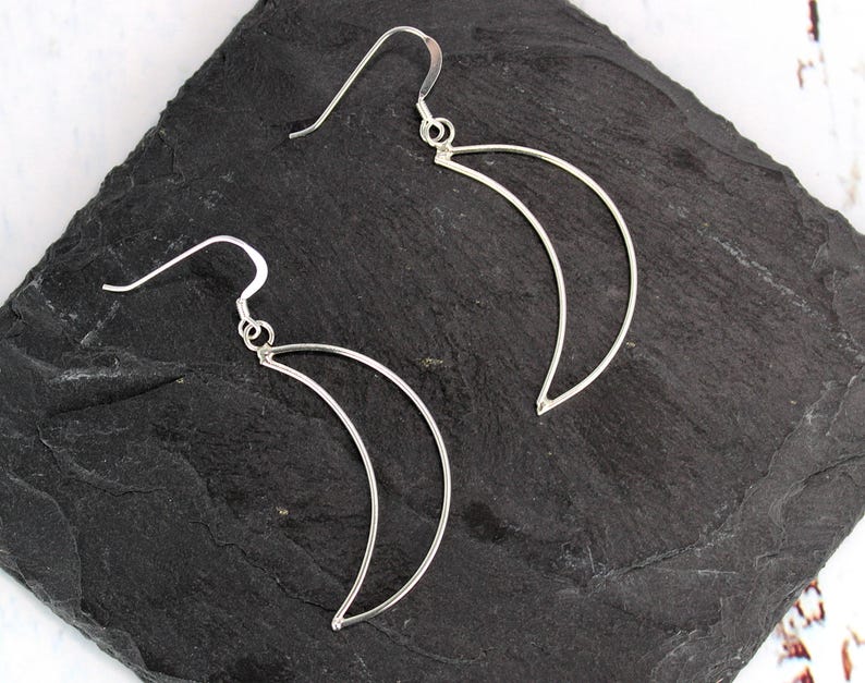May include: A pair of silver crescent moon earrings. The earrings are made of thin wire and have a simple, elegant design.