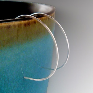May include: A pair of thin, silver-colored hoop earrings with a smooth, reflective finish. The circular metal bands are positioned vertically, showcasing a simple, open design that maintains a consistent thickness throughout the entire circumference.