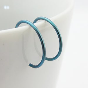 May include: A pair of teal blue hoop earrings. The earrings are made of metal and have a smooth finish.