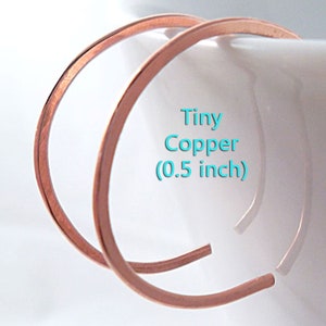 May include: Two small, open copper hoop earrings. The text on the image reads "Tiny Copper (0.5 inch)". The earrings are a warm, reddish-brown color and appear to be handmade. The hoops are thin and have a simple, minimalist design.
