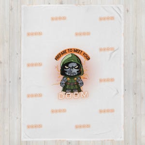Puede incluir: Manta de felpa blanca con una ilustración de dibujos animados del Doctor Doom y el texto "PREPARE TO MEET YOUR DOOM". La manta tiene la palabra "DOOM" repetida. El personaje está representado en verde y plata.