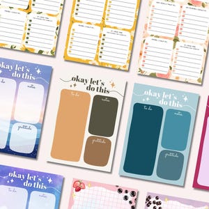 May include: A collection of colorful notepads with various designs and text. Some notepads feature floral patterns and the text "A Reluctant To-Do List." Other notepads have the text "okay let's do this" with sections for to-do lists, notes, and gratitude.