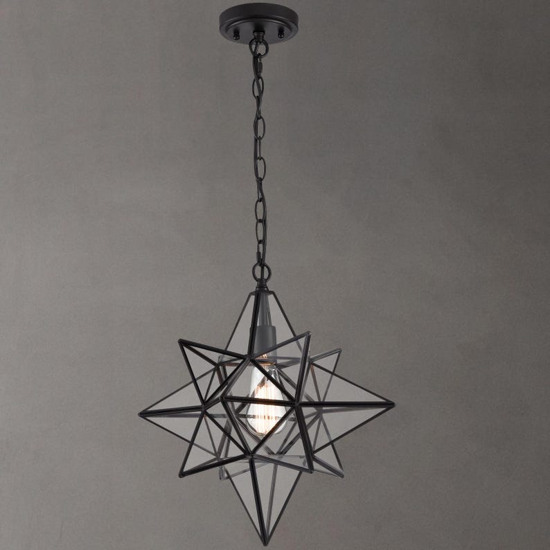 May include: Black metal star-shaped pendant light with a clear glass shade. The light is hanging from a chain.