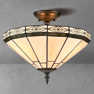May include: A semi-flush mount ceiling light fixture featuring a wide, inverted conical shade made of cream-colored glass panels with dark metal framing. The fixture includes a decorative bronze-toned canopy and a matching finial at the base.