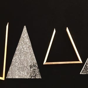 May include: Five gold-colored triangles of varying sizes, with two of the triangles filled with a sparkly, silver-colored material.