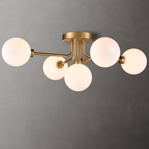 May include: A modern ceiling light fixture with five spherical white glass shades. The fixture has a brass finish and is mounted on a gray background. The light fixture is a stylish addition to any home.