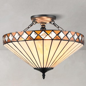 Può includere: Un lampadario decorativo con paralume in vetro colorato. Il paralume presenta un motivo geometrico di vetro ambrato, trasparente e bianco. Il lampadario ha una base e una catena in metallo color bronzo.
