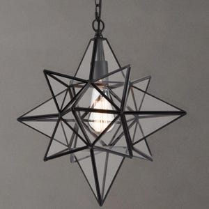 May include: Black metal star-shaped pendant light with clear glass panels. The light fixture has a geometric design and is suspended from a chain.