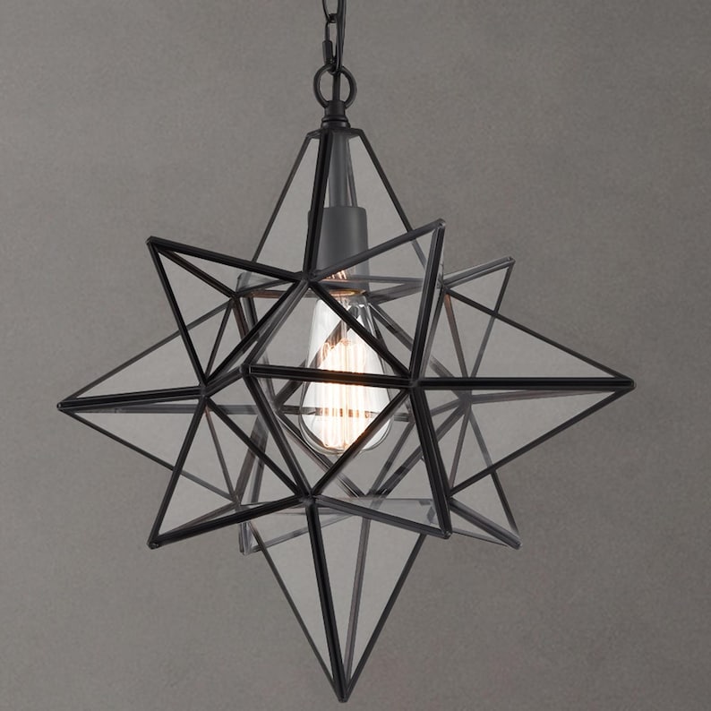 May include: Black metal star-shaped pendant light with clear glass panels. The light fixture has a geometric design and is suspended from a chain.