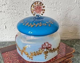 White and blue opaline jar/trinket dish with lid, decorated with gilt and pink wreaths, bows and florals.