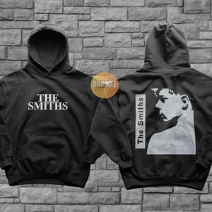 May include: Black hooded sweatshirt with a white graphic print of the band "The Smiths" on the front and a white graphic print of a person's face with the text "The Smiths" on the back.