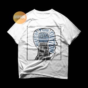 May include: White t-shirt featuring a graphic design with the text "PUSH THE BUTTON" in blue and white, along with a fist and a head silhouette. The shirt also includes the text "chemical brothers".