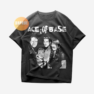 Op de afbeelding: Donkergrijs t-shirt met een zwart-wit afbeelding van de band Ace of Base. De naam van de band is in grote witte letters boven de afbeelding van de bandleden gedrukt. Het shirt heeft een ronde hals.