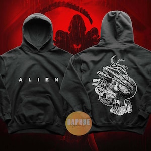 Puede incluir: Sudadera con capucha negra con la palabra "ALIEN" en letras blancas en la parte delantera. La parte trasera de la sudadera con capucha presenta un gráfico blanco detallado de la cabeza de una criatura. La sudadera con capucha tiene una capucha y un bolsillo delantero. El logotipo de Daphne Apparel es visible.
