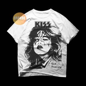May include: White t-shirt featuring a black and white graphic of Ace Frehley from the band KISS. The KISS logo is above the image, and "Ace Frehley" is printed below. The shirt has short sleeves and a crew neck.