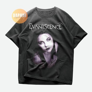 May include: Dark gray t-shirt featuring the band name "Evanescence" in white script above a grayscale portrait of a woman. The shirt is a crew neck style.