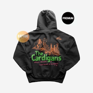 May include: A dark grey hooded sweatshirt with a green and orange graphic print of the band "The Cardigans" and the text "Erase/ Rewind (2008 Remix by Kleerup)".