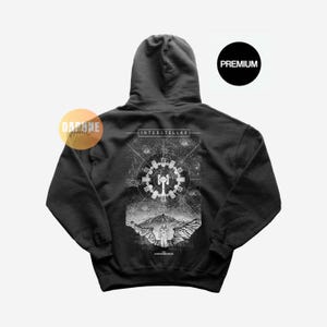 Op de afbeelding: Een zwarte hoodie met een witte grafische print op de achterkant. Het ontwerp toont de tekst INTERSTELLAR boven een ruimtestation, een berglandschap en een astronautfiguur. De tekst CHRISTOPHER NOLAN staat onderaan afgebeeld.