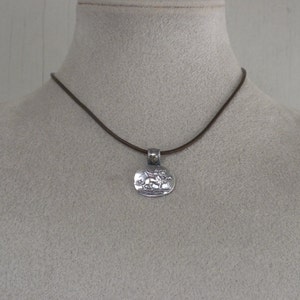 May include: A silver pendant necklace with a brown leather cord. The pendant features a detailed design of two figures.