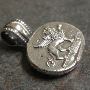May include: Silver pendant featuring a detailed winged lion, a symbol of Venice, Italy. The pendant has a textured surface and a loop for attaching a chain.