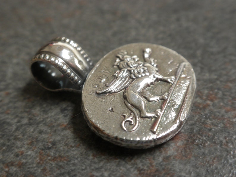 May include: Silver pendant featuring a detailed winged lion, a symbol of Venice, Italy. The pendant has a textured surface and a loop for attaching a chain.