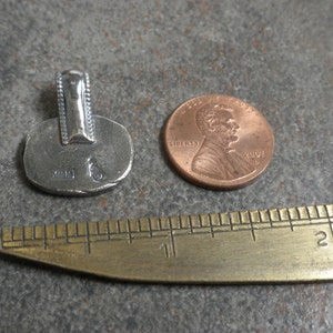 May include: Silver pendant with a textured surface and a bail. The pendant is about the size of a US penny.