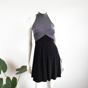 May include: A black and silver halter dress on a mannequin. The top is silver with horizontal stripes, and the skirt is black. The dress has a high neckline and a flared skirt. The mannequin is on a white background.