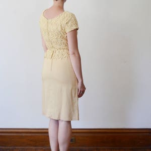 Puede incluir: Un vestido de encaje amarillo con falda ajustada y mangas cortas. El vestido est&aacute; hecho de una tela delicada y tiene una silueta femenina.