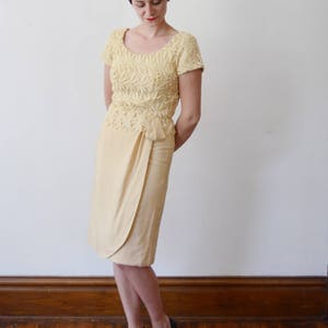 Puede incluir: Una mujer con un top de encaje amarillo y una falda amarilla a juego. Est&aacute; de pie sobre un suelo de madera y tiene el pelo corto y casta&ntilde;o.
