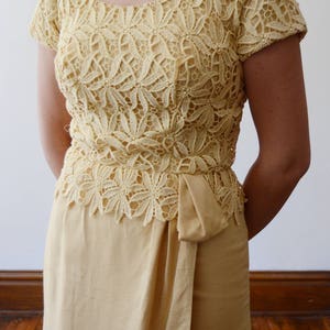 Puede incluir: Un vestido amarillo p&aacute;lido con un corpi&ntilde;o de encaje y una falda lisa. El corpi&ntilde;o de encaje tiene un escote redondo y mangas cortas. La falda es de estilo envolvente con un lazo en la cintura.