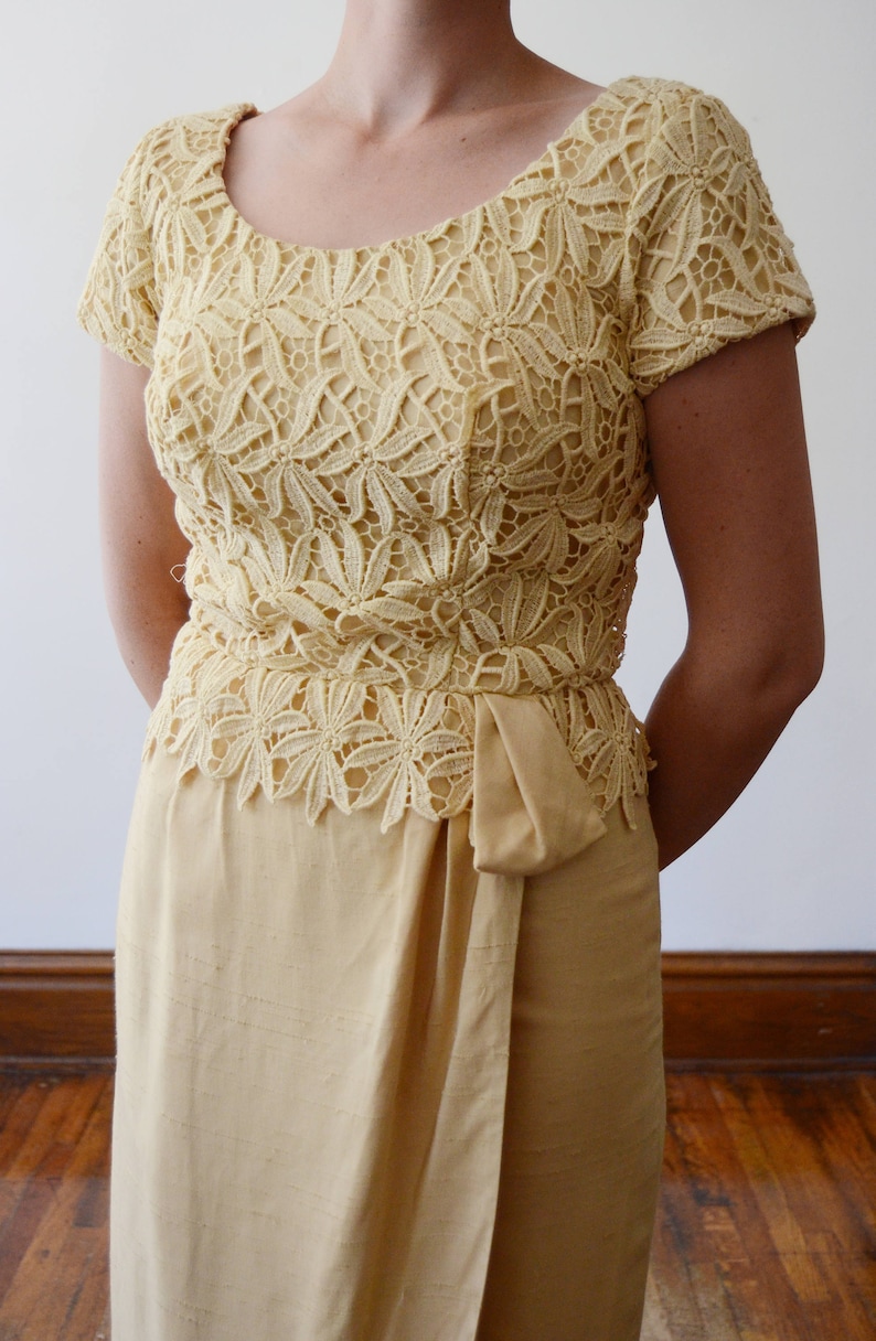 Puede incluir: Un vestido amarillo p&aacute;lido con un corpi&ntilde;o de encaje y una falda lisa. El corpi&ntilde;o de encaje tiene un escote redondo y mangas cortas. La falda es de estilo envolvente con un lazo en la cintura.