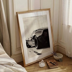 Peut inclure: Impression en noir et blanc d'une voiture de sport classique, encadr&eacute;e dans un cadre dor&eacute;. L'image montre l'arri&egrave;re et le c&ocirc;t&eacute; de la voiture sur une route. Le cadre est pos&eacute; contre un mur.