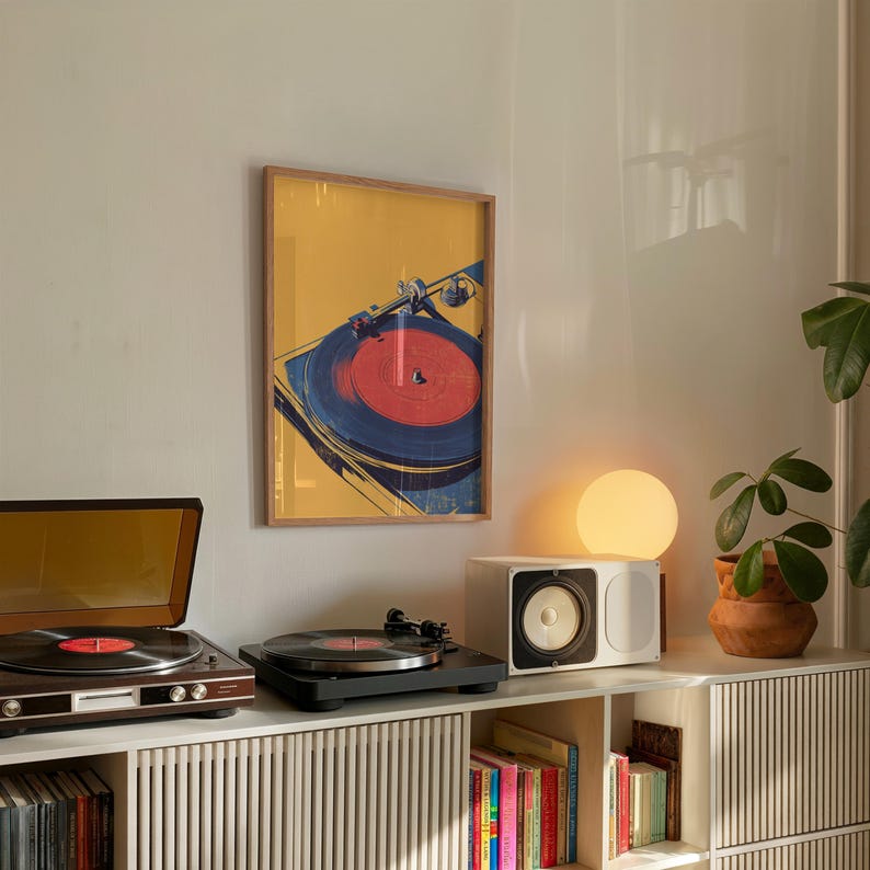 May include: A framed wall art print featuring a stylized illustration of a vinyl record player with a red record on a yellow background. The artwork is displayed above a wooden cabinet containing two record players, a speaker, and books.
