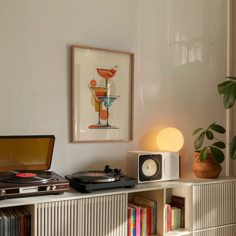 May include: A framed wall art print featuring a vertical illustration of three stacked cocktail glasses in red, yellow, and blue hues, displayed above a wooden media console with a record player, a white speaker, and a glowing spherical lamp.