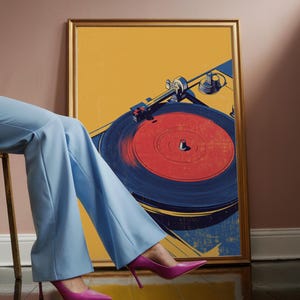 May include: A framed rectangular wall art print featuring a stylized graphic illustration of a record player with a red vinyl record. The artwork uses a color palette of mustard yellow, deep blue, and red, encased in a thin gold-toned frame.