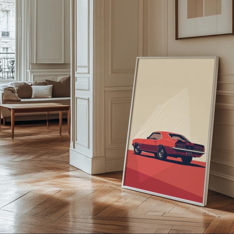 May include: A framed art print featuring a stylized illustration of a red muscle car viewed from the rear three-quarter angle. The car is set against a minimalist background with a light beige upper section and a solid red lower ground plane.