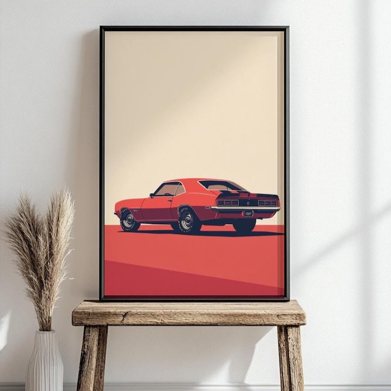 May include: A framed wall art print featuring a stylized illustration of a red muscle car viewed from the rear three-quarter angle. The car has black racing stripes, dark wheels, and is set against a solid cream background with a red ground plane.