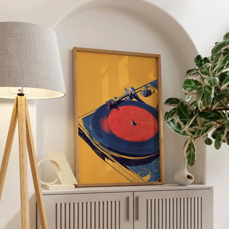 May include: A rectangular framed wall art print featuring a stylized illustration of a record player. The artwork displays a vibrant yellow background with a dark blue turntable and a bright red vinyl record centered on the platter.