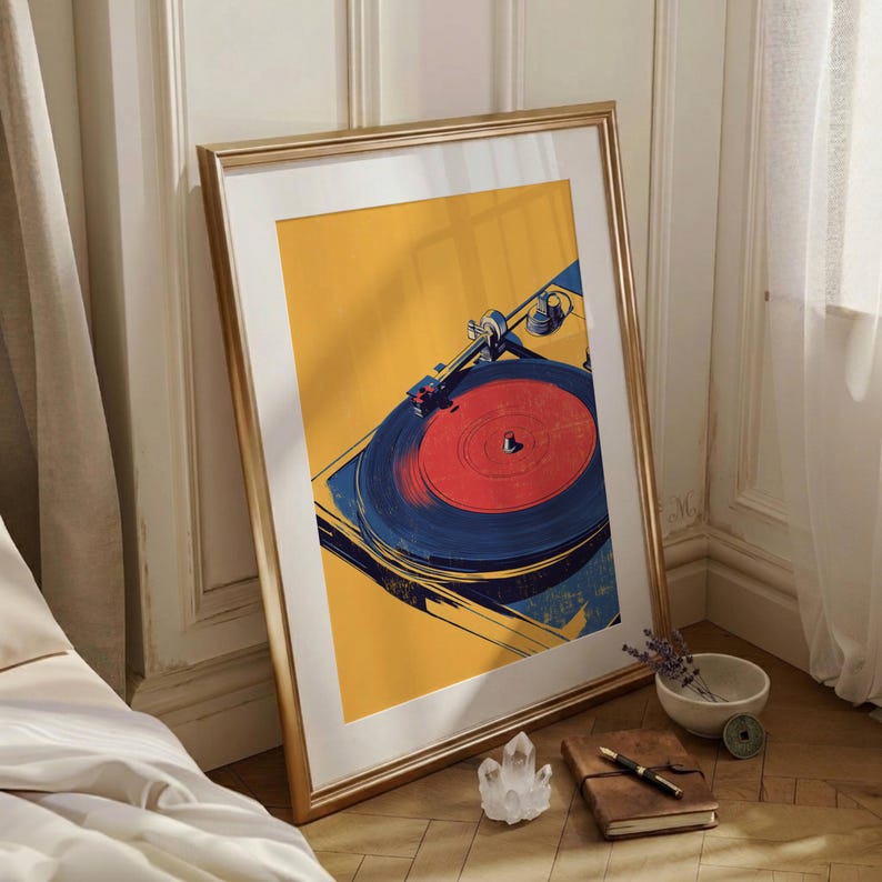 May include: A framed art print featuring a stylized illustration of a record player. The artwork displays a vibrant yellow background with a dark blue turntable and a bright red vinyl record. The frame is metallic gold with a white mat border.