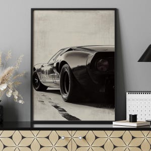 Peut inclure: Impression encadr&eacute;e en noir et blanc d'une voiture de sport classique. L'&oelig;uvre repr&eacute;sente l'arri&egrave;re de la voiture, mettant en valeur son design &eacute;pur&eacute; et ses gros pneus. L'impression a une esth&eacute;tique vintage, avec un fond textur&eacute; et un cadre noir.