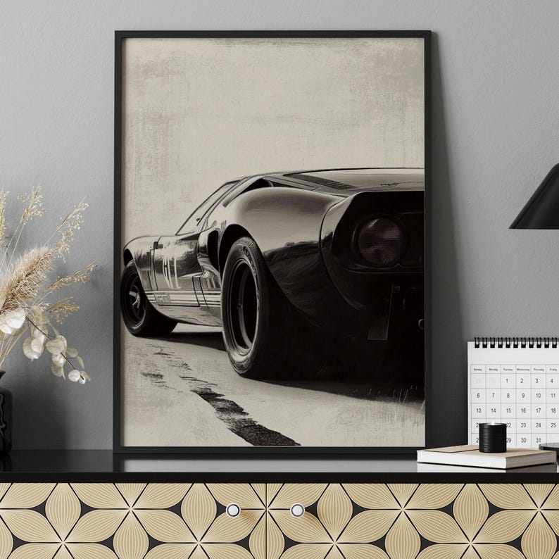 Peut inclure: Impression encadr&eacute;e en noir et blanc d'une voiture de sport classique. L'&oelig;uvre repr&eacute;sente l'arri&egrave;re de la voiture, mettant en valeur son design &eacute;pur&eacute; et ses gros pneus. L'impression a une esth&eacute;tique vintage, avec un fond textur&eacute; et un cadre noir.