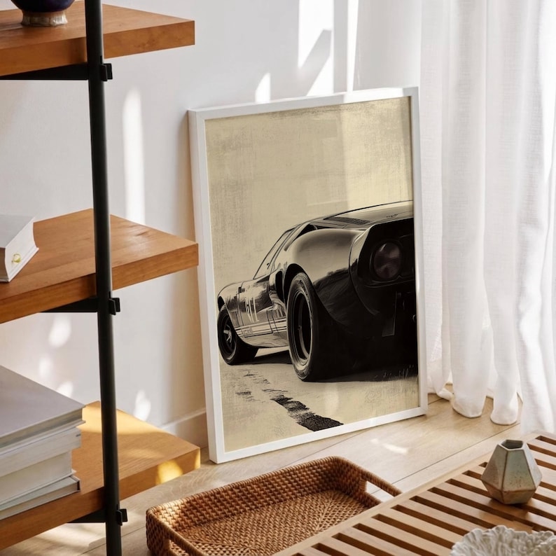 Peut inclure: Impression d'art encadr&eacute;e repr&eacute;sentant une voiture de sport noire vintage. La voiture est vue d'en bas, mettant en valeur son design &eacute;l&eacute;gant et ses gros pneus. Le fond est beige neutre et l'impression est dans un cadre blanc. L'&oelig;uvre est expos&eacute;e sur un sol en bois.