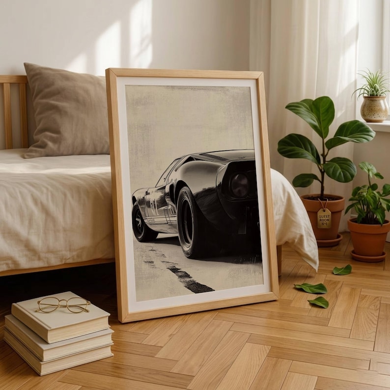 Peut inclure: Impression encadr&eacute;e d'une voiture de sport noire vintage, vue de l'arri&egrave;re, mettant en valeur son design &eacute;l&eacute;gant et ses gros pneus. L'&oelig;uvre est en s&eacute;pia, avec une bande noire sur la route. L'impression est dans un cadre en bois clair.