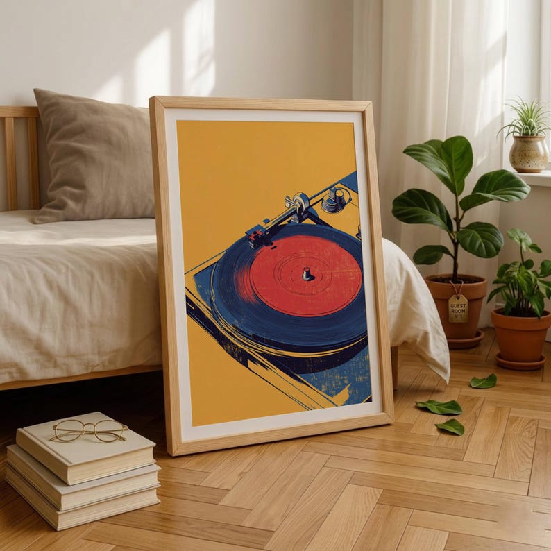 May include: A framed art print featuring a stylized illustration of a record player with a vibrant red vinyl record on a dark blue platter, set against a solid mustard yellow background. The artwork is displayed in a light wood frame.