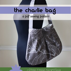 Może przedstawiać: Szara i biała torba typu tote z tkaniny z wzorem liści. Torba wisi na czarnym manekinie. Tekst "the charlie bag" i "a pdf sewing pattern" jest wyświetlany nad torbą. Tekst "olive tree textiles" jest wyświetlany pod torbą.