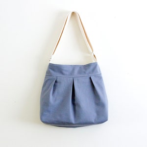 May include: A gray canvas tote bag with a white strap. The bag has a pleated design and a wide opening.